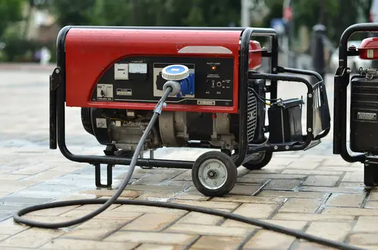 Portable red generator on a paved surface with a power cable plugged in