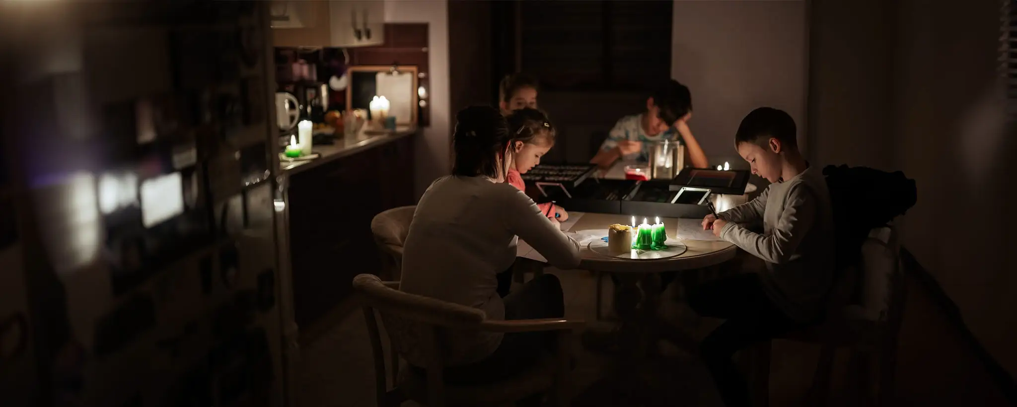 Family sitting together at a candlelit kitchen table during a power outage