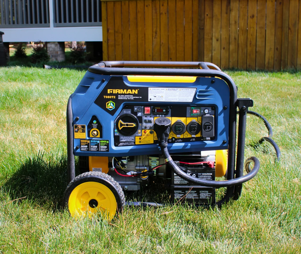 Firman T08072 tri-fuel portable generator on a lawn, showing the control panel with outlets, switches, and wattage labels.