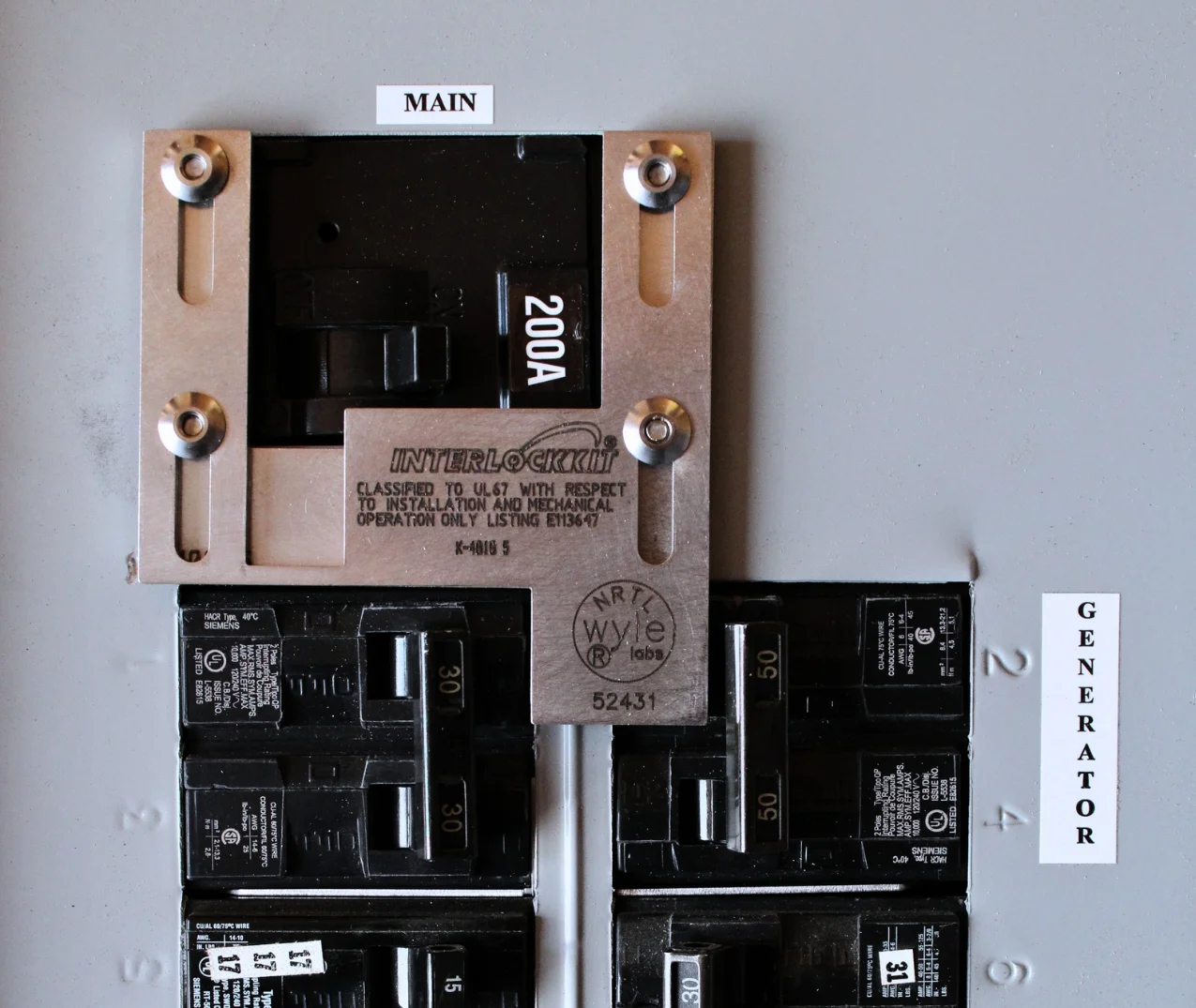 A residential electrical breaker panel showing a 200A main breaker with a stainless steel Interlockkit interlock device installed, next to a 50A generator breaker labeled "GENERATOR."